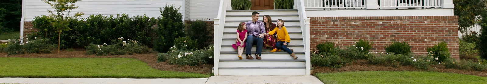 Image of family smiling on the steps of a large house