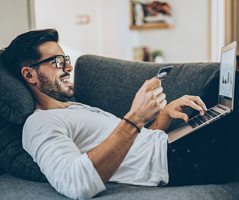 Young man using credit card and laptop on couch