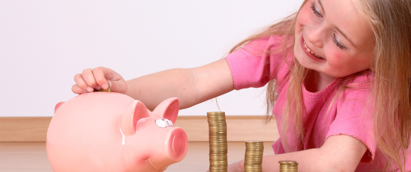 Little girl putting coins into a piggy bank