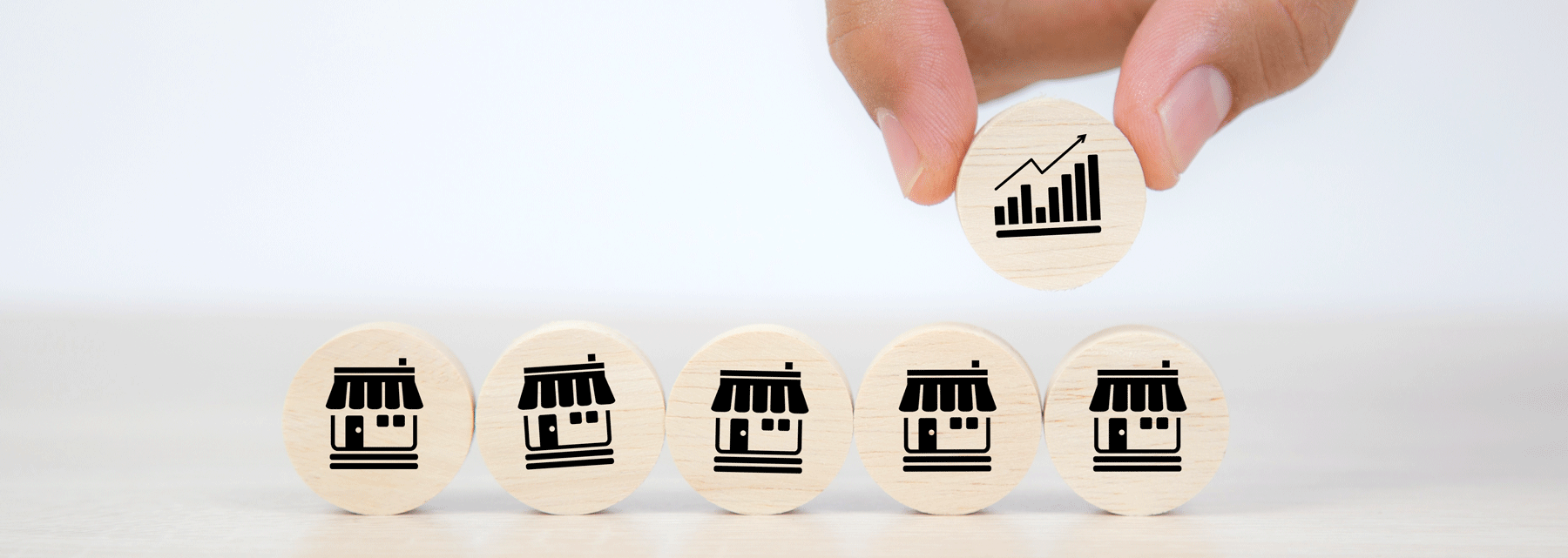 5 wooden coins with a storefront and a human hand bringing down a 6th chip with growth bars in the midst of them.